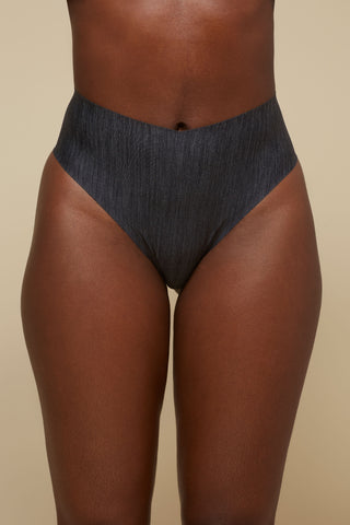 Front view image of model wearing Netherlin's black seamless high rise thong, made of aerated, quick-drying fabric and embedded with mineral fibers to inhibit odor and bacteria.