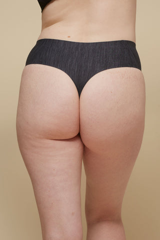 Rear view image of model wearing Netherlin's black seamless high rise thong, made of aerated, quick-drying fabric and embedded with mineral fibers to inhibit odor and bacteria.