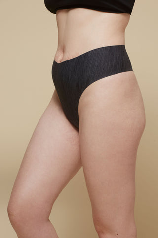 Side view image of model wearing Netherlin's black seamless high rise thong, made of aerated, quick-drying fabric and embedded with mineral fibers to inhibit odor and bacteria.