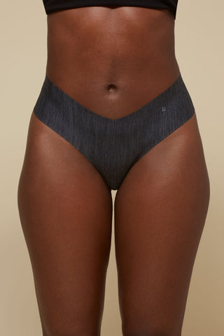 Front view image of model wearing Netherlin's black seamless mid rise thong, made of aerated, quick-drying fabric and embedded with mineral fibers to inhibit odor and bacteria.