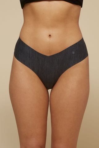 Front view image of model wearing Netherlin's black seamless mid rise thong, made of aerated, quick-drying fabric and embedded with mineral fibers to inhibit odor and bacteria.