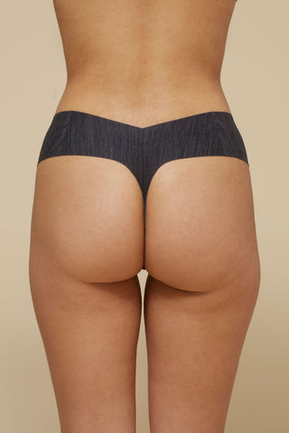 Rear view image of model wearing Netherlin's black seamless mid rise thong, made of aerated, quick-drying fabric and embedded with mineral fibers to inhibit odor and bacteria.