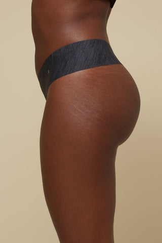 Side view image of model wearing Netherlin's black seamless mid rise thong, made of aerated, quick-drying fabric and embedded with mineral fibers to inhibit odor and bacteria.
