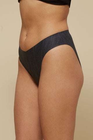Side view image of model wearing Netherlin's black seamless french cut brief, made of aerated, quick-drying fabric and embedded with mineral fibers to inhibit odor and bacteria.