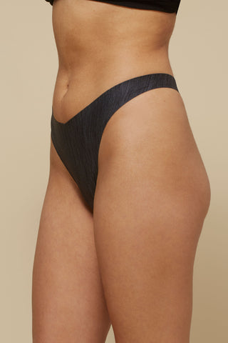 Side view image of model wearing Netherlin's black seamless thong with extra thin waistband, made of aerated, quick-drying fabric and embedded with mineral fibers to inhibit odor and bacteria.